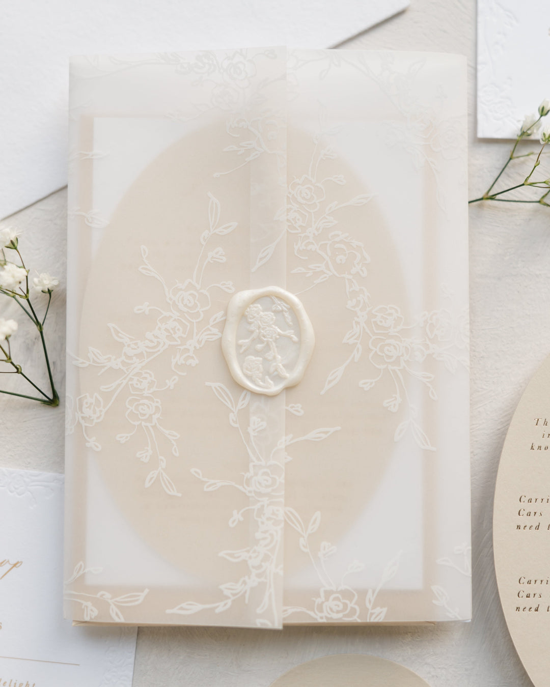 Beige card inside floral vellum wrap with pearl white wax seal on a light surface