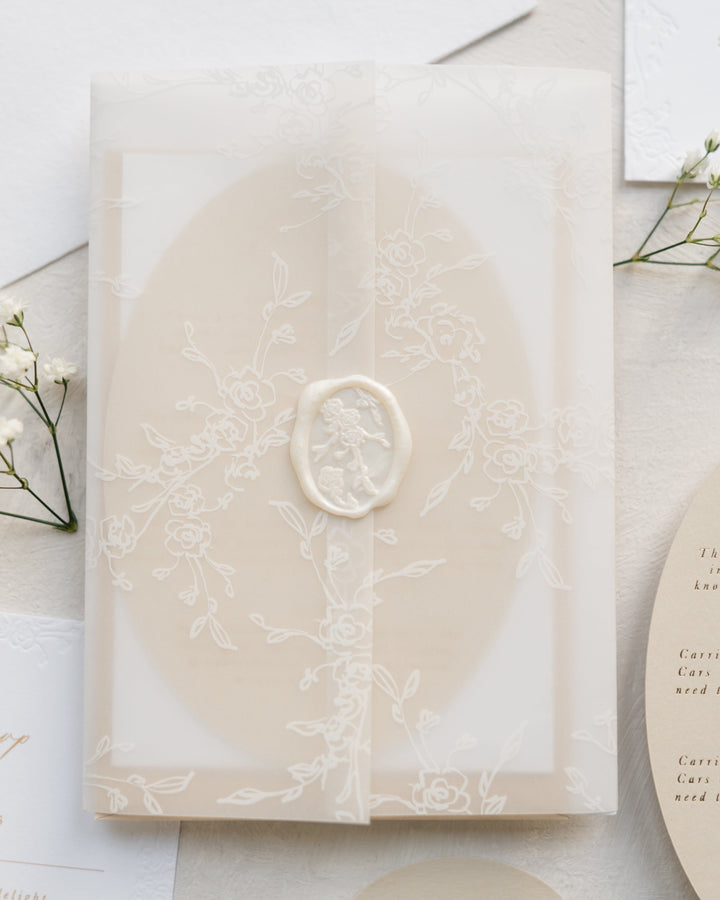 Beige card inside floral vellum wrap with pearl white wax seal on a light surface