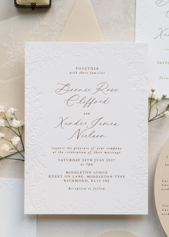 Luxury debossed wedding invitation with floral border and gold pressed foil on light background