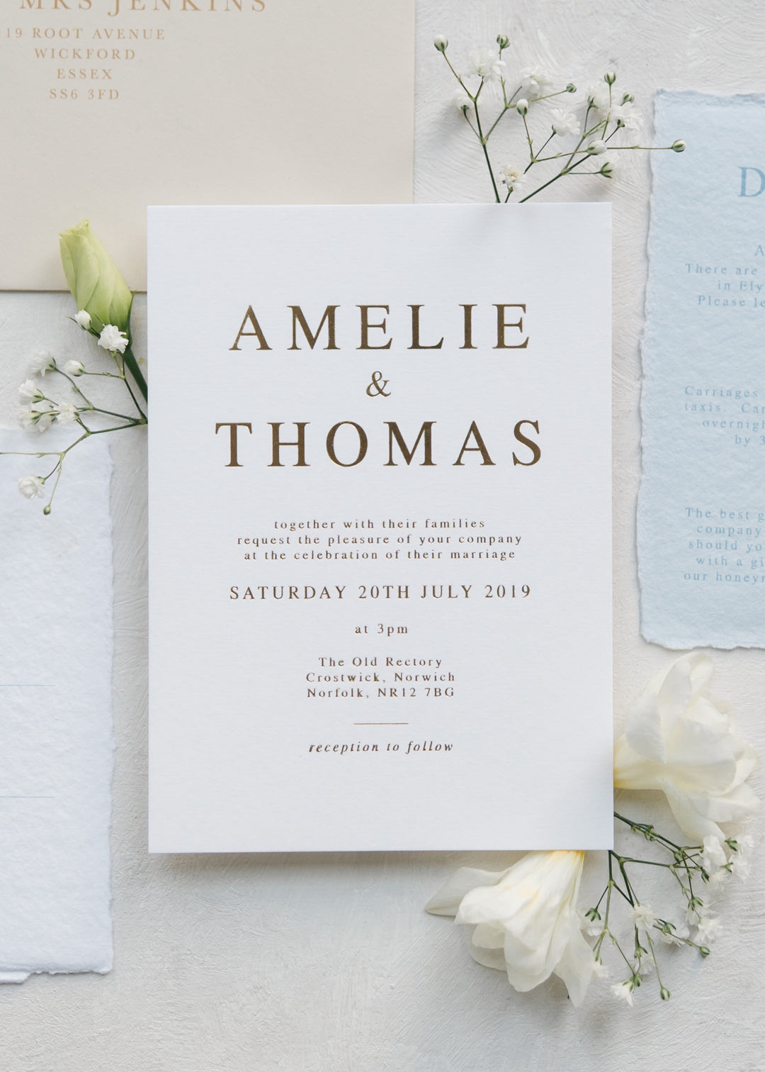 Gold foil bold text invitation on white card on a light background with flowers