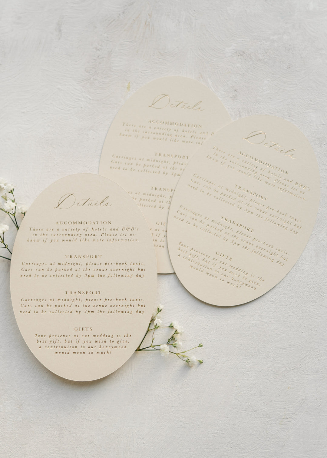 Three oval wedding details cards in beige on a light background with small white flowers.