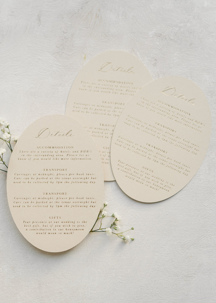 Three oval wedding details cards in beige on a light background with small white flowers.